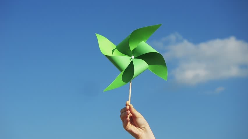 A vibrant, colorful spin wheel in a hand against a blue sky. green energy concept. A green pinwheel spins joyfully in the breeze. Renewable non-polluting energy sources, environment