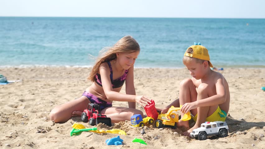 Brother and sister play on the beach with plastic toys with sand.Children are playing on the beach. Summer water fun for the whole family. A boy and a girl are playing with sand on the seashore.