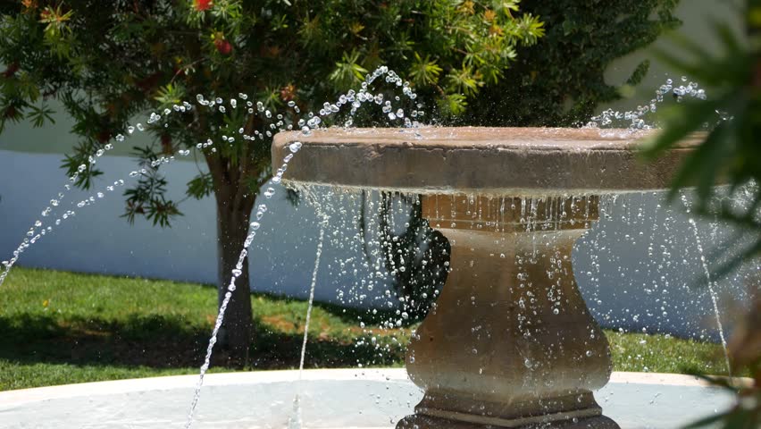 Fountain close-up. Drops of water fall on a stone in the sunlight. Splashes flow steam high quality 4K video. Los Jardines del Marquesado de la Quinta Roja, La Orotava, Tenerife.