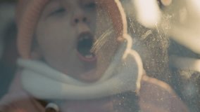 A close-up of a young girl wearing a pink knit hat and white scarf, blowing air onto a foggy car window. Her breath creates condensation on the glass - Powered by Shutterstock - Get 15% off with code: PIKWIZARD15