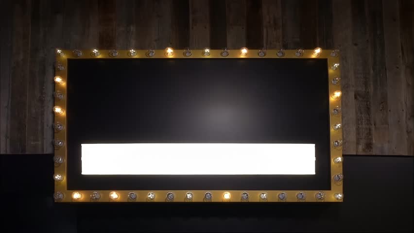 A vintage-style rectangular marquee sign bordered by exposed light bulbs, mounted against a rustic wooden wall. The center is black with an illuminated white strip.