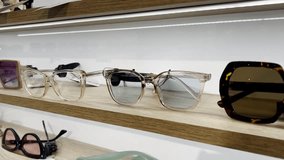 A collection of stylish modern eyeglasses and sunglasses displayed on a wooden shelf in a store. The showcased glasses include various designs and colors, catering to different preferences. - Powered by Shutterstock - Get 15% off with code: PIKWIZARD15