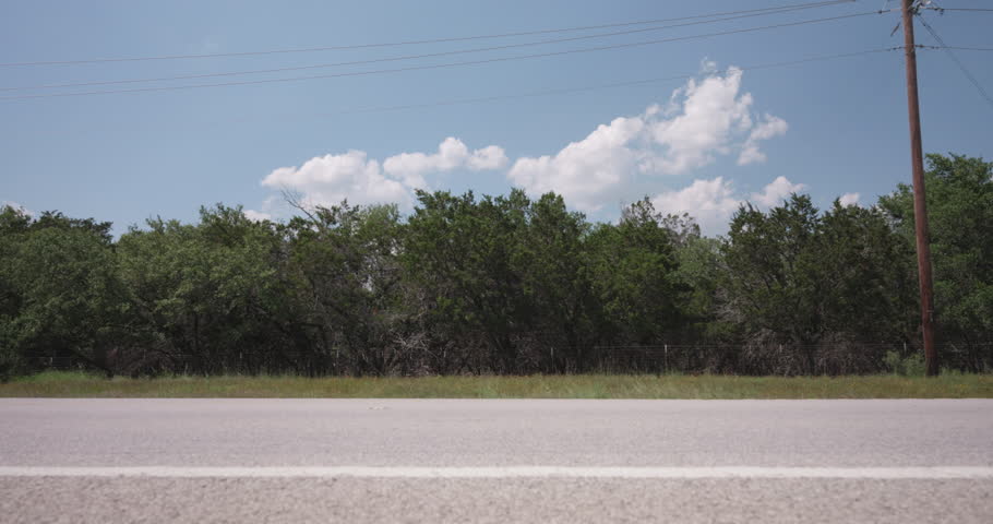 A black truck drives along a sunny summer highway in the Texas Hill Country - slider left to right