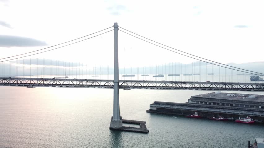 The aerial view from a drone reveals the Bay Bridge along the Embarcadero in San Francisco, highlighting urban space and historic architecture against the backdrop of the San Francisco Bay.