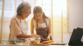 4K Happy Asian family senior mother and adult daughter enjoy and fun healthy lifestyle learning to cook and making vegan food salad by watching online class recipe on digital tablet in the kitchen. - Powered by Shutterstock - Get 15% off with code: PIKWIZARD15
