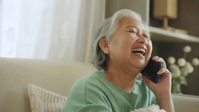 Happy Asian senior mature woman relaxing on sofa in living room speaking on mobile phone with family. Elderly grandmother enjoy smart indoor lifestyle with wireless technology and digital device. - Powered by Shutterstock - Get 15% off with code: PIKWIZARD15