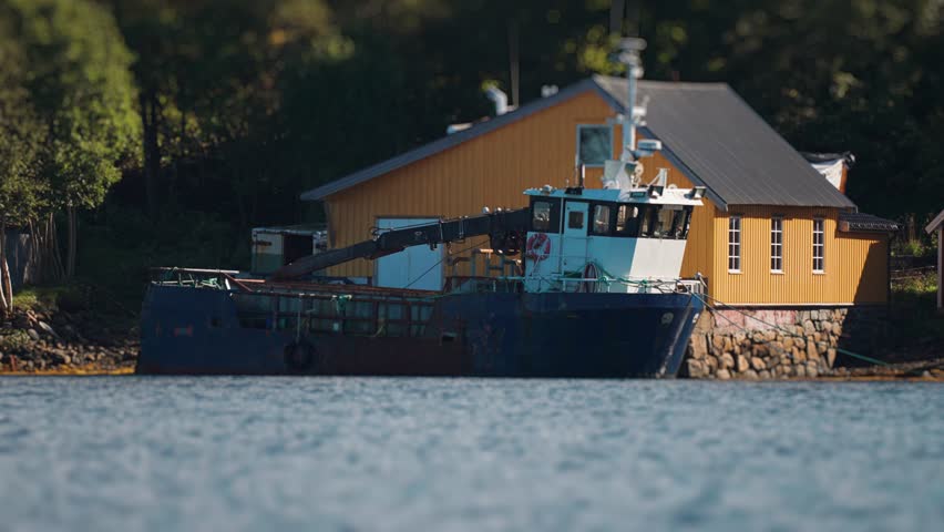 Scenic view of a blue boat moored by a yellow boat-house, with a peaceful waterfront setting.