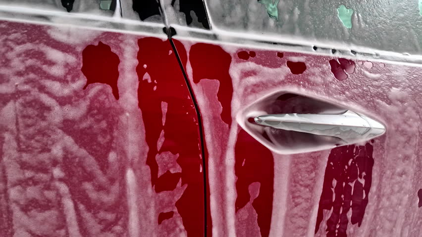 Red car exterior covered in foam at wash process carwash, aluminium door handles