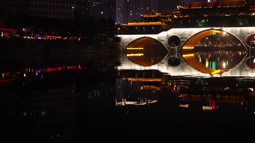 tilt up view at night of Chengdu capital city of the Chinese province of Sichuan, Anshun Bridge over the Jin river with modern skyline skyscraper building