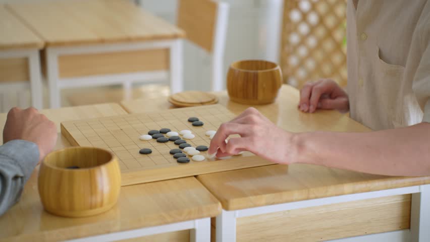 Close up of young men play board game Go during competition in community. Attractive two male friend players participate in traditional asian chinese board game match on table in the club house center
