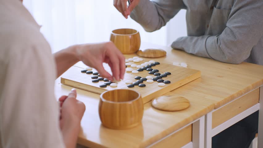 Close up of young men play board game Go during competition in community. Attractive two male friend players participate in traditional asian chinese board game match on table in the club house center