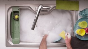 A man is scrubbing dishes in a bright kitchen, immersed in his task with bubbles and colorful kitchenware around him. - Powered by Shutterstock - Get 15% off with code: PIKWIZARD15