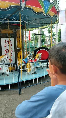 Back view of a boy is looking at a merry-go-round horse that is running but there are no passengers because it only operates at night.