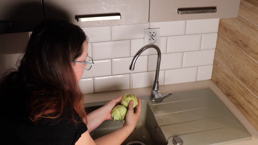 A woman’s hands clean Green Kohlrabi turnip in the sink. 