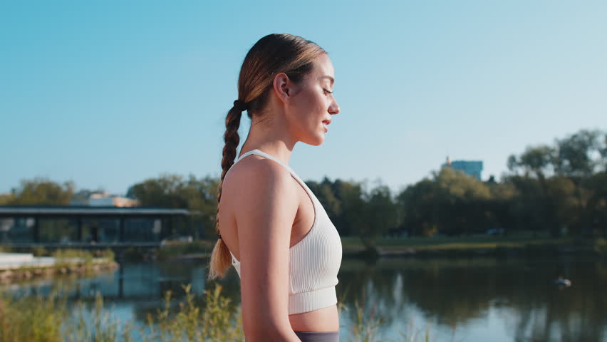 Side view of athletic fitness sport runner girl training, putting on wireless headphones and listening favorite music song. Workout cardio in morning city park. Young woman jogging healthy lifestyle.