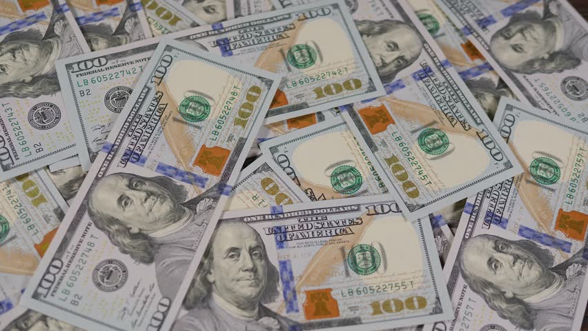 A close-up of a white-gloved hand placing a gold bitcoin coin on hundred-dollar bills. Digital money, banking, investment, finance and business concept.