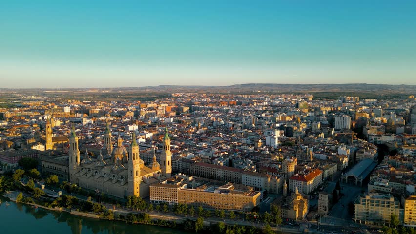 Aerial view of Zaragoza skyline. Drone going forward above Ebro River close to Cathedral of Zaragoza. Sunset point with orange reflections. Travel destination in Aragon - Spain