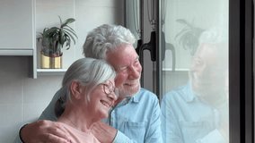 Serene elderly couple at home looking out the window hugging, taking care of each other and smiling, authentic retirement lifestyle - Powered by Shutterstock - Get 15% off with code: PIKWIZARD15