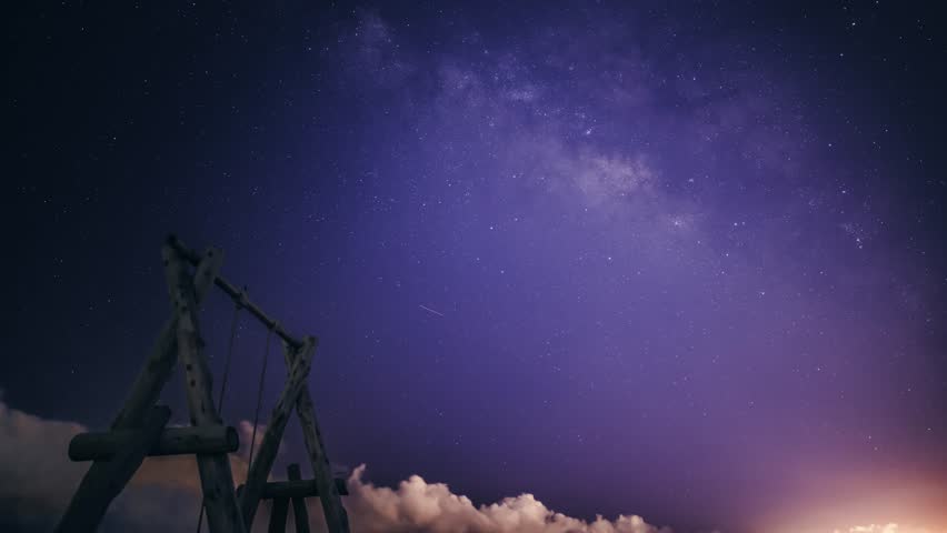 The Milky Way stretches across the night sky. A solitary wooden swing set stands on a sandy beach, inviting viewers to imagine swinging under the vast, starry sky. Zhuangwei, Yilan County, Taiwan.