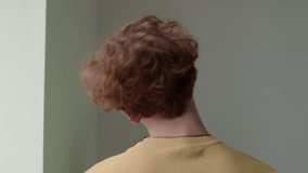 Rear view of red curly haired guy slowly rotating head, warming up neck and relieving pain indoors - Powered by Shutterstock - Get 15% off with code: PIKWIZARD15