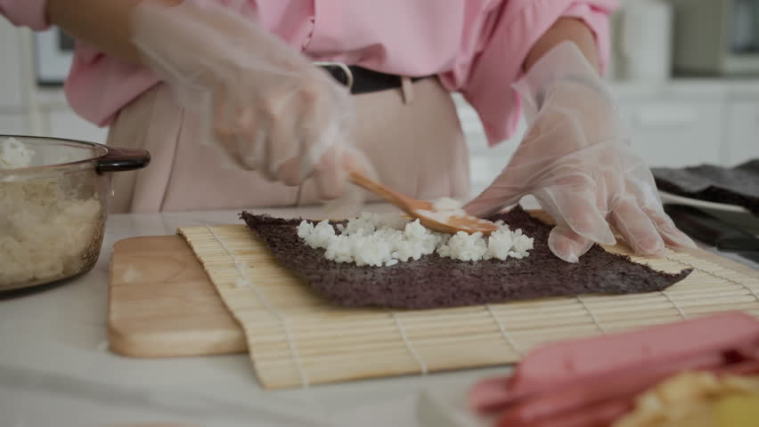 Cropped shot of anonymous woman placing rice on nori while cooking kimbap on kitchen counter