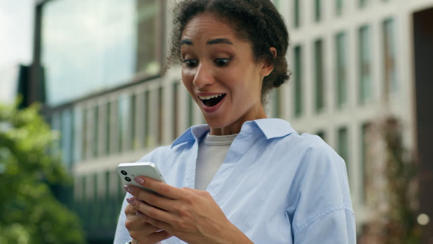 African American student girl female entrepreneur business woman lady manager businesswoman in city outside outdoors amazed wonder typing mobile phone smiling good news smartphone message win online