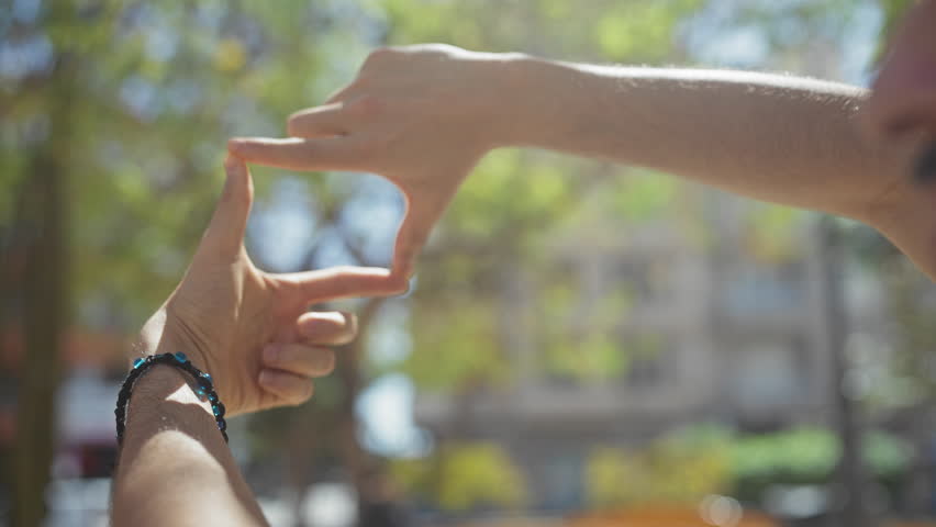 Bearded man framing perspective with hands in a sunny urban park setting.