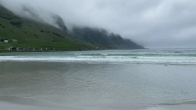 Waves gently lap against the sandy beach at Vågsøy, Norway, with moody foggy mountains and colorful wooden houses providing a picturesque backdrop - Powered by Shutterstock - Get 15% off with code: PIKWIZARD15