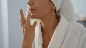 Woman applying lip balm in spa room wearing white robe and towel, capturing self-care and relaxation indoors - Powered by Shutterstock - Get 15% off with code: PIKWIZARD15