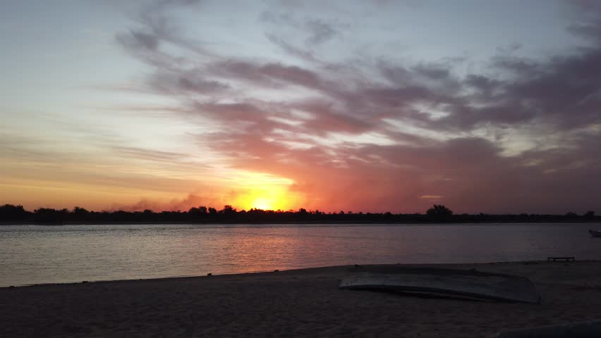Small motorboat slowly drives in river bay sunset with a nostalgic sky landscape and a old canoe laying on the sand, panoramic view
