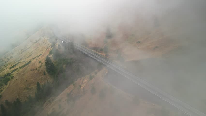 Aerial through low clouds above highway 95 in White Bird Idaho in low dry grassy mountains in summer