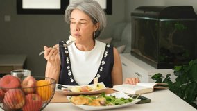 Senior woman enjoying a healthy lunch while reading a book in her home kitchen. The apples and indoor plants create a cozy, relaxed atmosphere - Powered by Shutterstock - Get 15% off with code: PIKWIZARD15