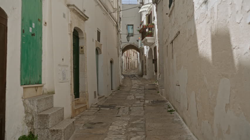 Young hispanic woman walking through the charming narrow streets of ostuni old town in puglia, italy, showcasing traditional european architecture.