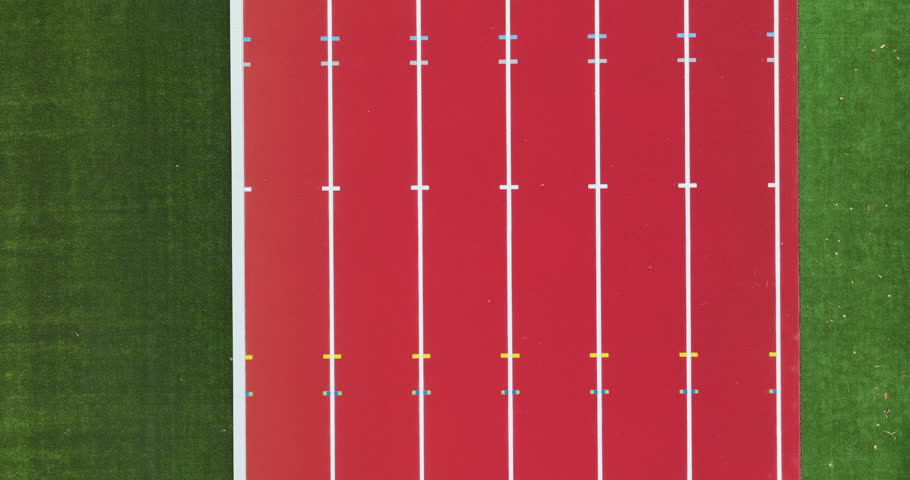 This aerial perspective showcases a vibrant red athletic track contrasted against lush green grass.