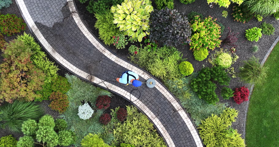A gardener works with pressure washer. Cleaning Garden Brick Made Paths. Aerial View.