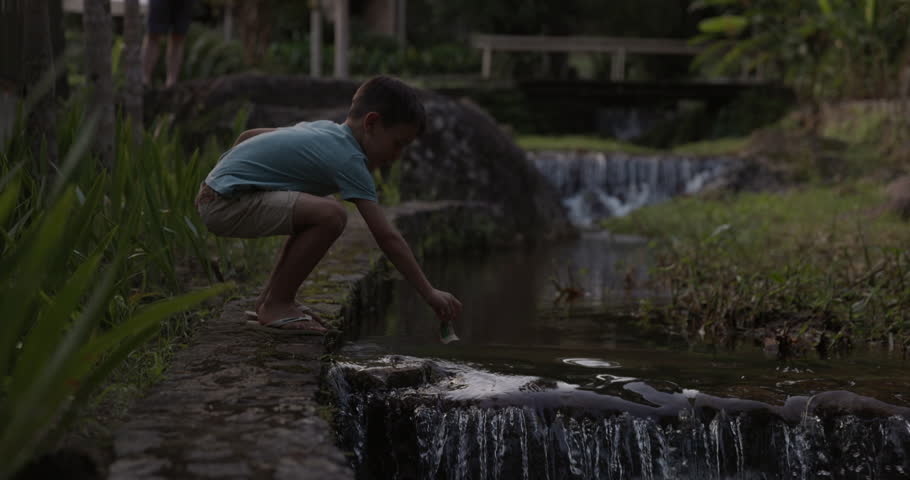 Young boy puts paper boat in water just before water fall - young imagination and play