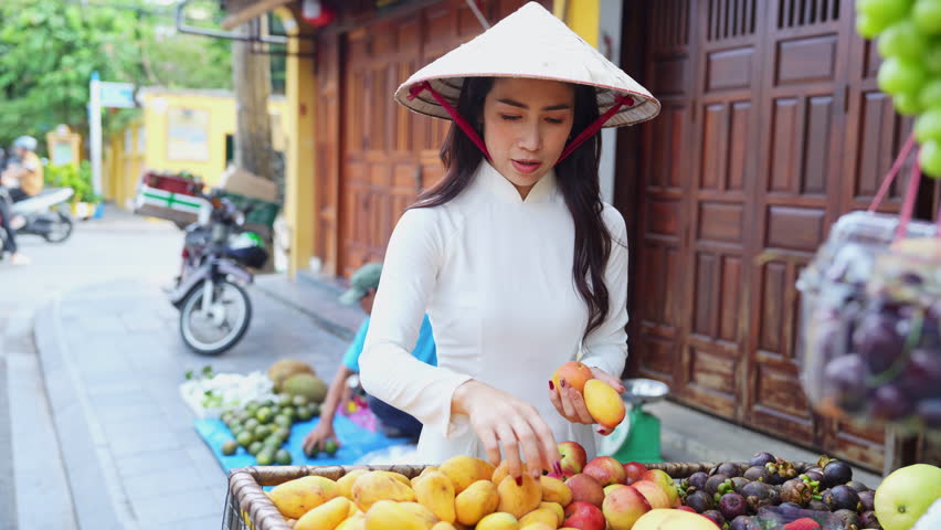 Asian woman wearing traditional Vietnamese culture and buying fruit in Hoi An walking street market in Vietnam