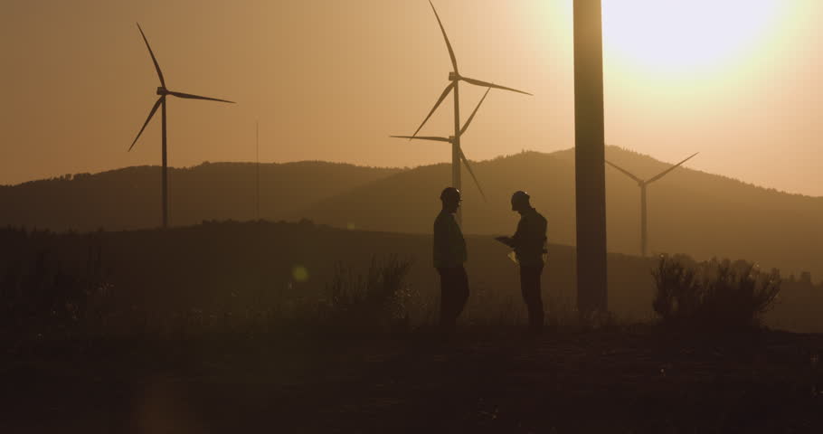 One engineer shows another engineer the information on the tablet. Sunset in the background