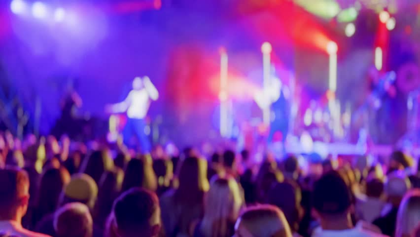 Large crowd is enjoying a vibrant concert with colorful lights and live music, creating an energetic and lively atmosphere.