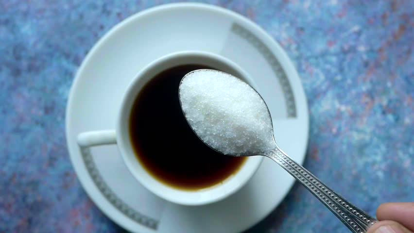 pouring white sugar in a tea cup 