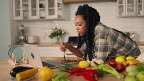 Lunchtime in home, African American girl using laptop, eating salad in kitchen. Young adult black woman watching TV series on notebook, when having dinner, healthy dietic food, vegetarian cuisine - Powered by Shutterstock - Get 15% off with code: PIKWIZARD15