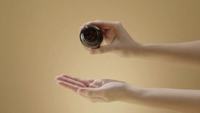Front commercial footage, many red and black medicine pills from blank label amber bottle held in a beautiful hand, being poured into the other hand palm. Front angle shot, beige background - Powered by Shutterstock - Get 15% off with code: PIKWIZARD15