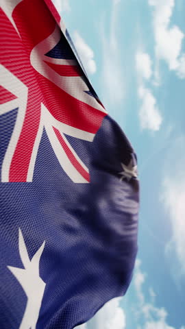 Wavy flag of Australia blowing in the wind in slow motion. Waving colorful Australian flag symbol abstract vertical video background. Sun and blue sky with clouds on a background