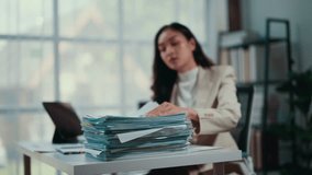 Stressed office worker flipping through numerous documents, feeling overwhelmed and tired at her desk in a modern, bright office environment - Powered by Shutterstock - Get 15% off with code: PIKWIZARD15