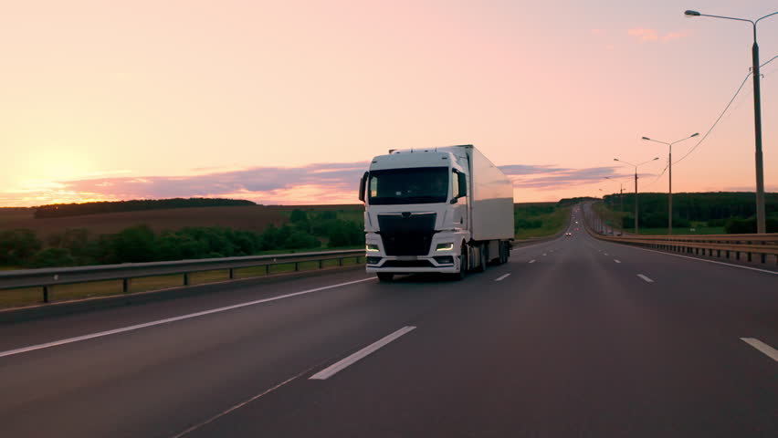 White truck with cargo trailer driving on intercity highway in countryside at sunset, logistics and delivery of goods by freight transportation.