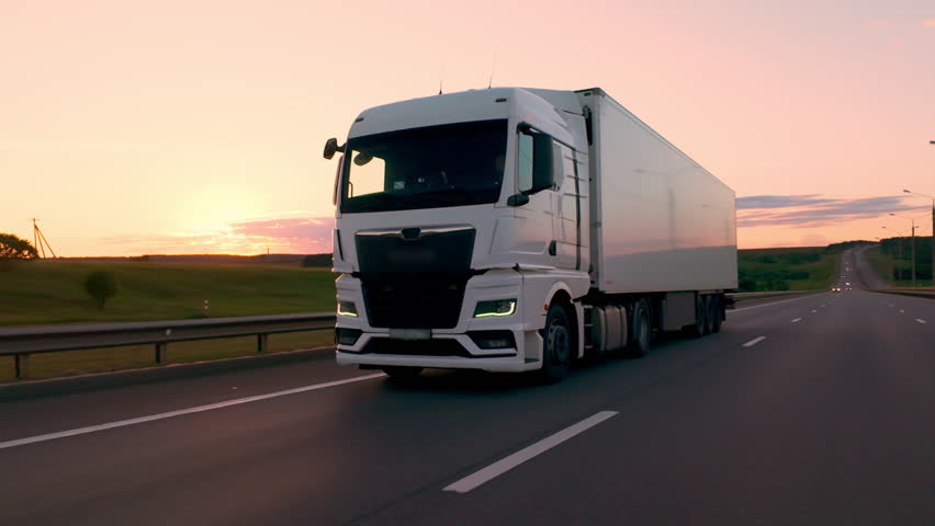 White truck with cargo trailer driving on intercity highway in countryside at sunset, logistics and delivery of goods by freight transportation.