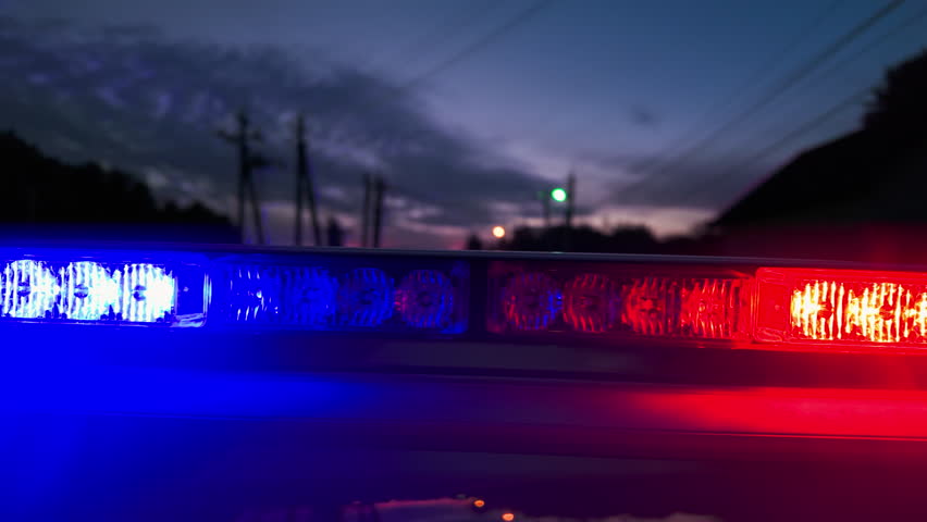 Police patrol car with red and blue flashing light driving along night street in countryside.