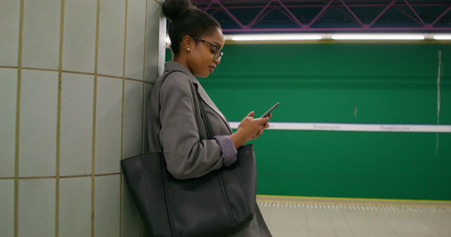 A woman in formal clothes uses a mobile phone while standing on a subway platform. There is no train