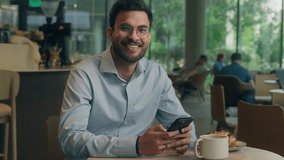 Arabian man ethnic muslim Indian businessman guy entrepreneur using mobile phone business lunch in cafe restaurant male visitor millennial tourist read message cellphone looking at camera happy smile - Powered by Shutterstock - Get 15% off with code: PIKWIZARD15