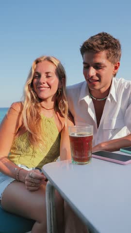 Vertical. Young couple sitting on the terrace of a beach bar, paying the bill with a credit card to the cashier.Two people giving a payment to the waiter after a good service. Client checkout at shore